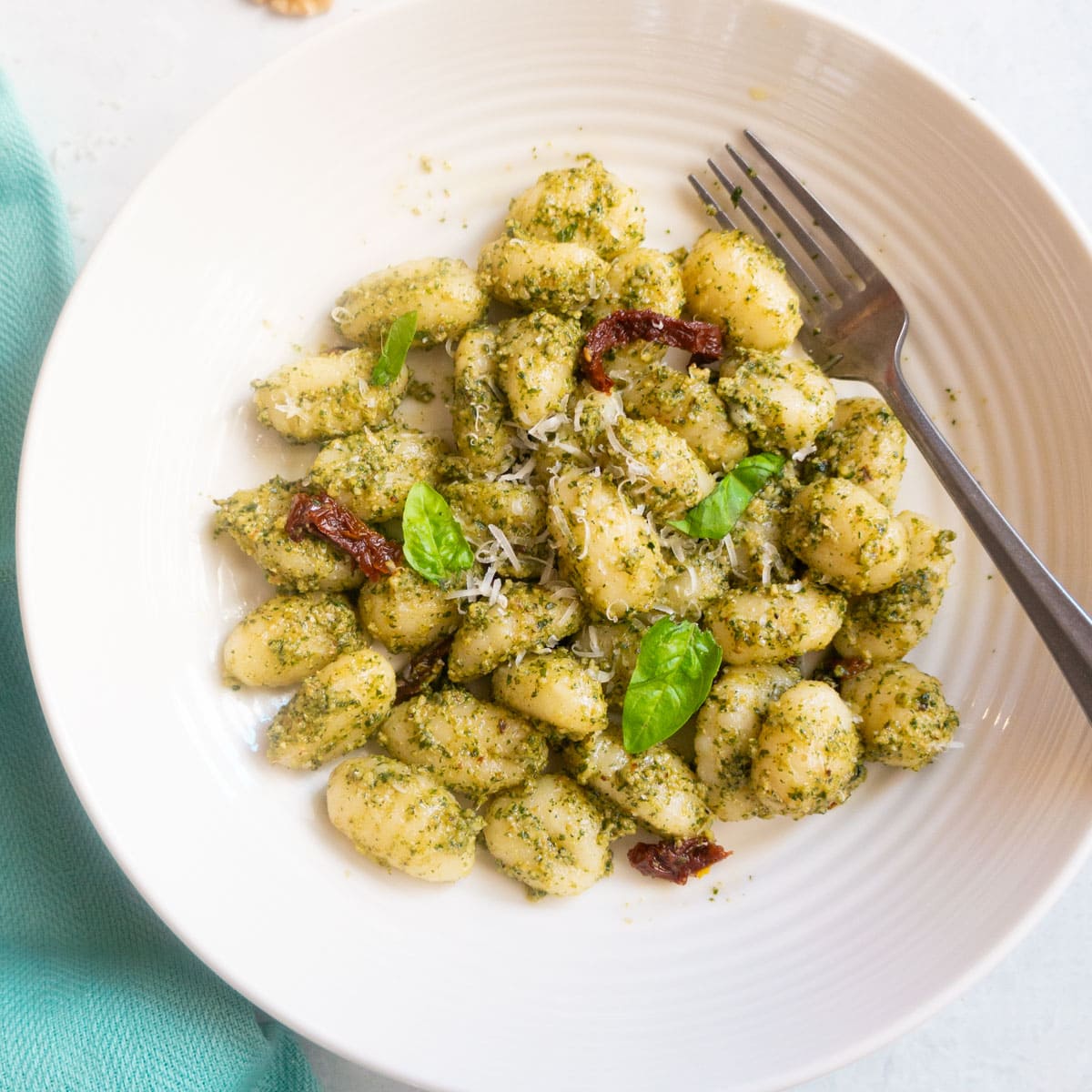 pesto Gnocchi in a white plate garnished with basil leaves and parmesan cheese