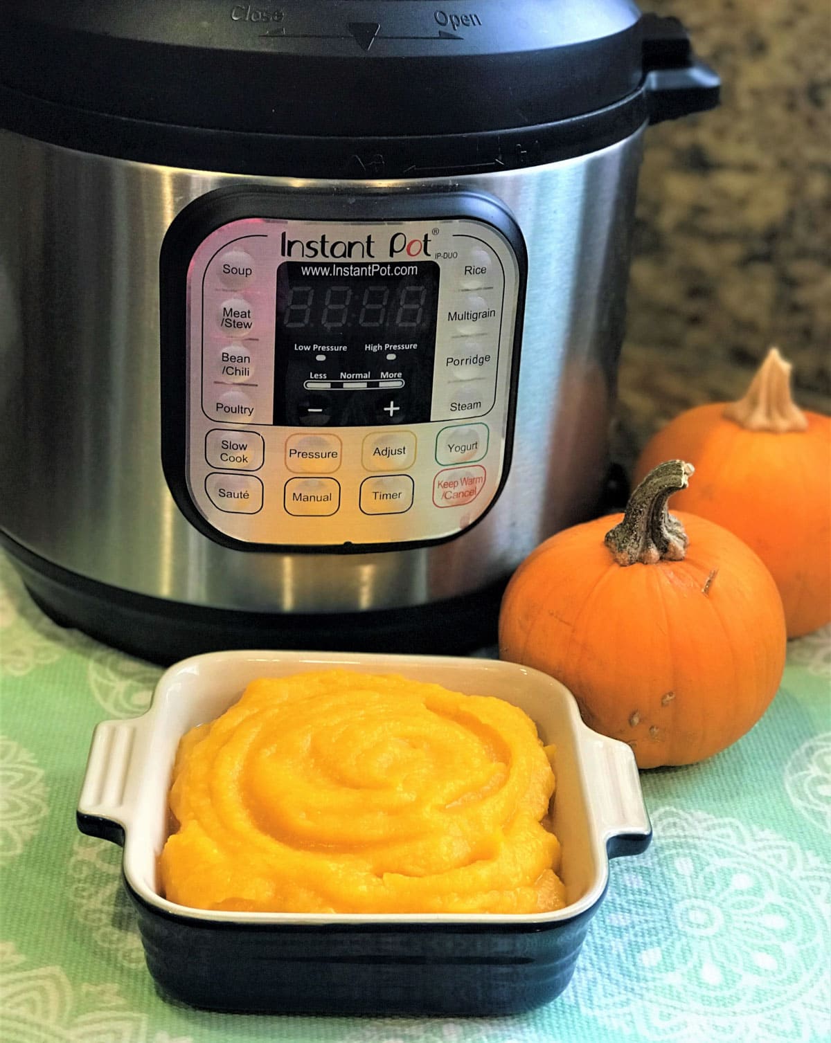 Pumpkin Puree in a square bowl in front of Instant Pot and whole pumpkin