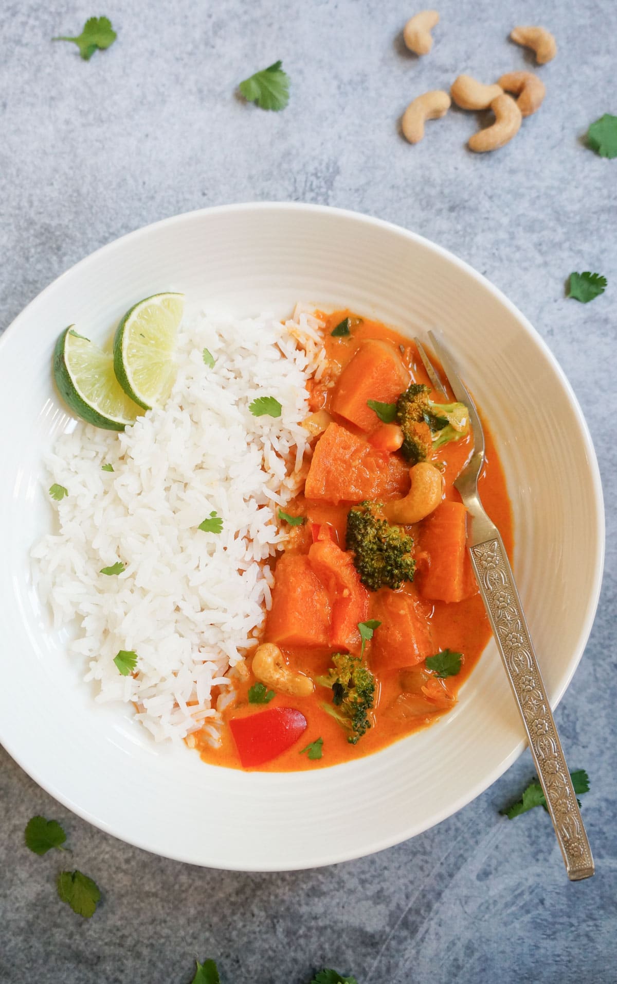 top view of thai pumpkin red curry in a plate with rice and lime slices