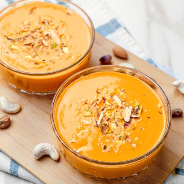 Two bowls of carrot kheer on a wooden board with cashews on side