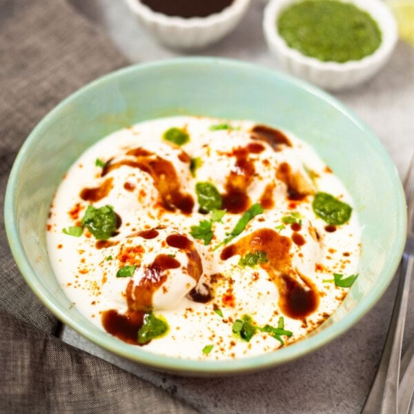 Dahi Vada in a green bowl topped with tamarind and green chutney