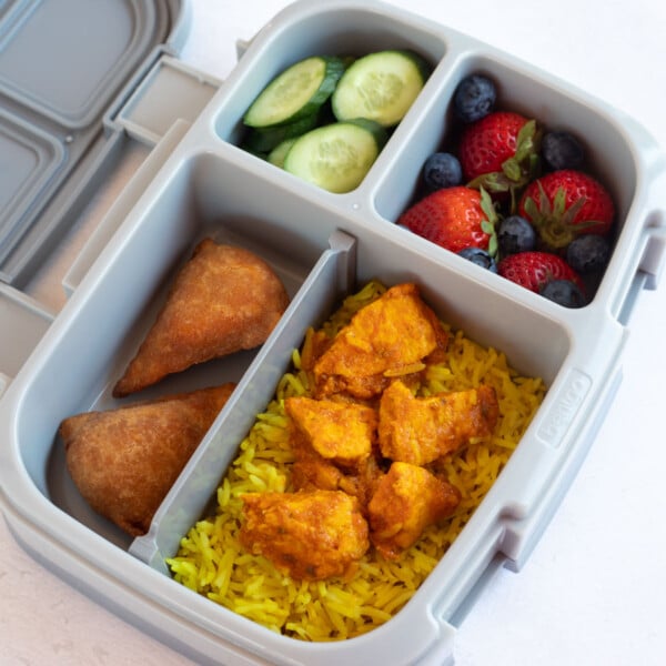 Indian inspired kids lunchbox with chicken and rice, berries and cucumbers.