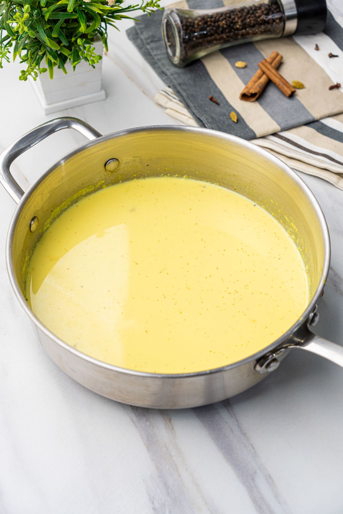 Golden Turmeric Milk in a pot with cinnamon sticks, black peppercorns and cloves at the back