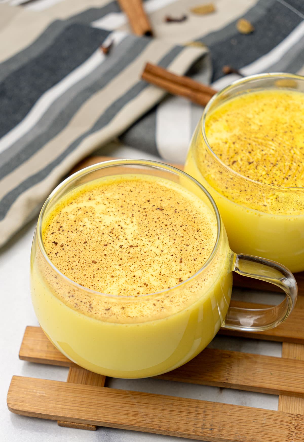 haldi doodh in two cups with cinnamon stick at the back