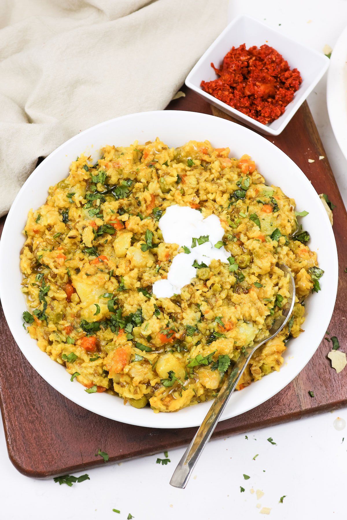 Ready to serve masala khichdi topped with yogurt in a white bowl