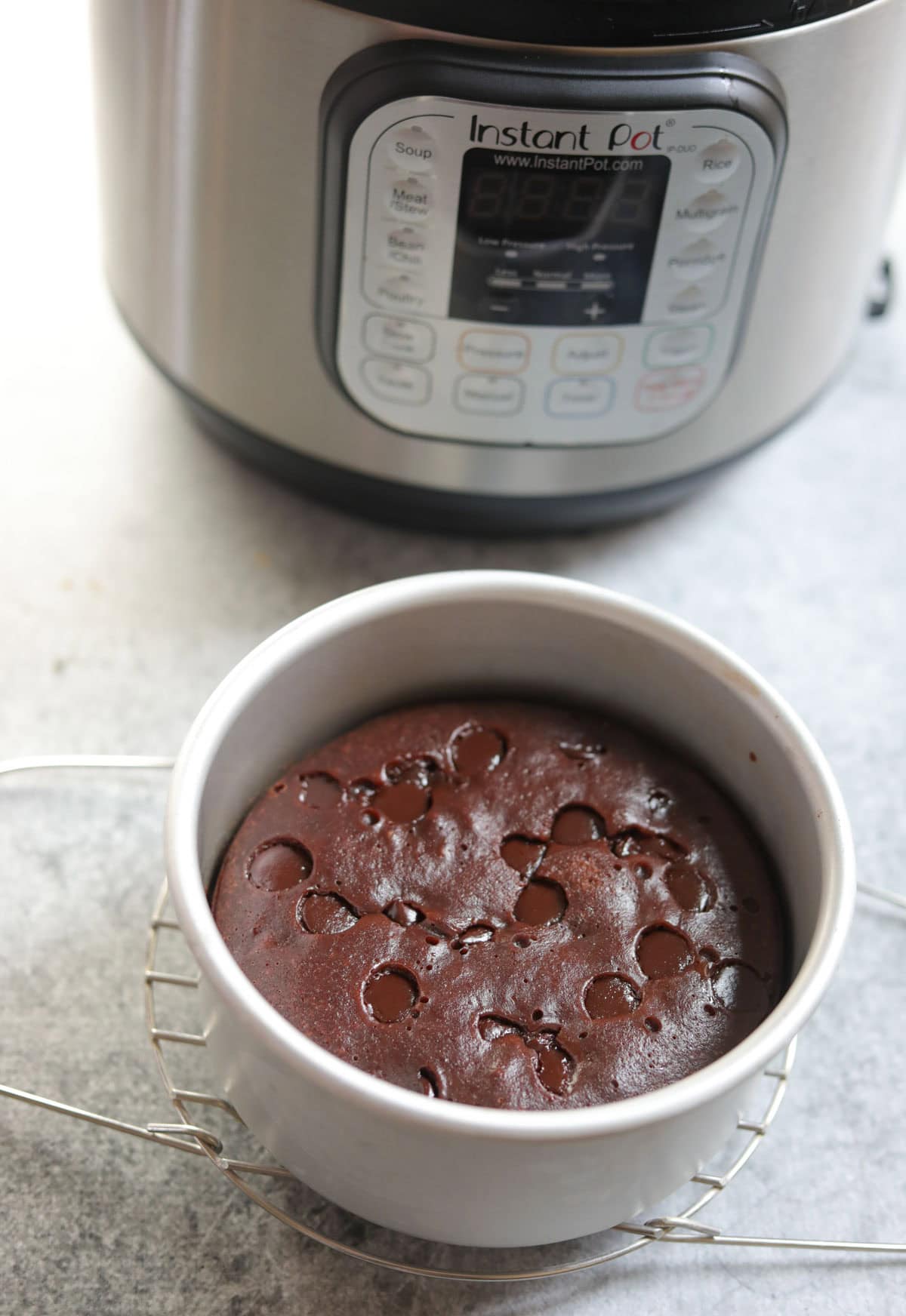 freshly cooked instant pot brownie in a white bowl with the Instant Pot at the background