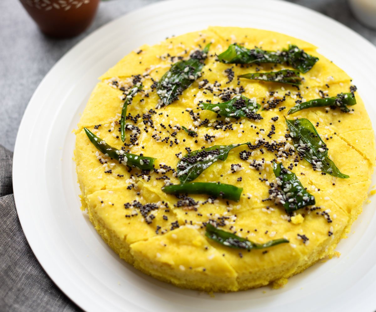 closeup shot of Khaman Dhokla garnished with tempering of curry leaves on a white plate