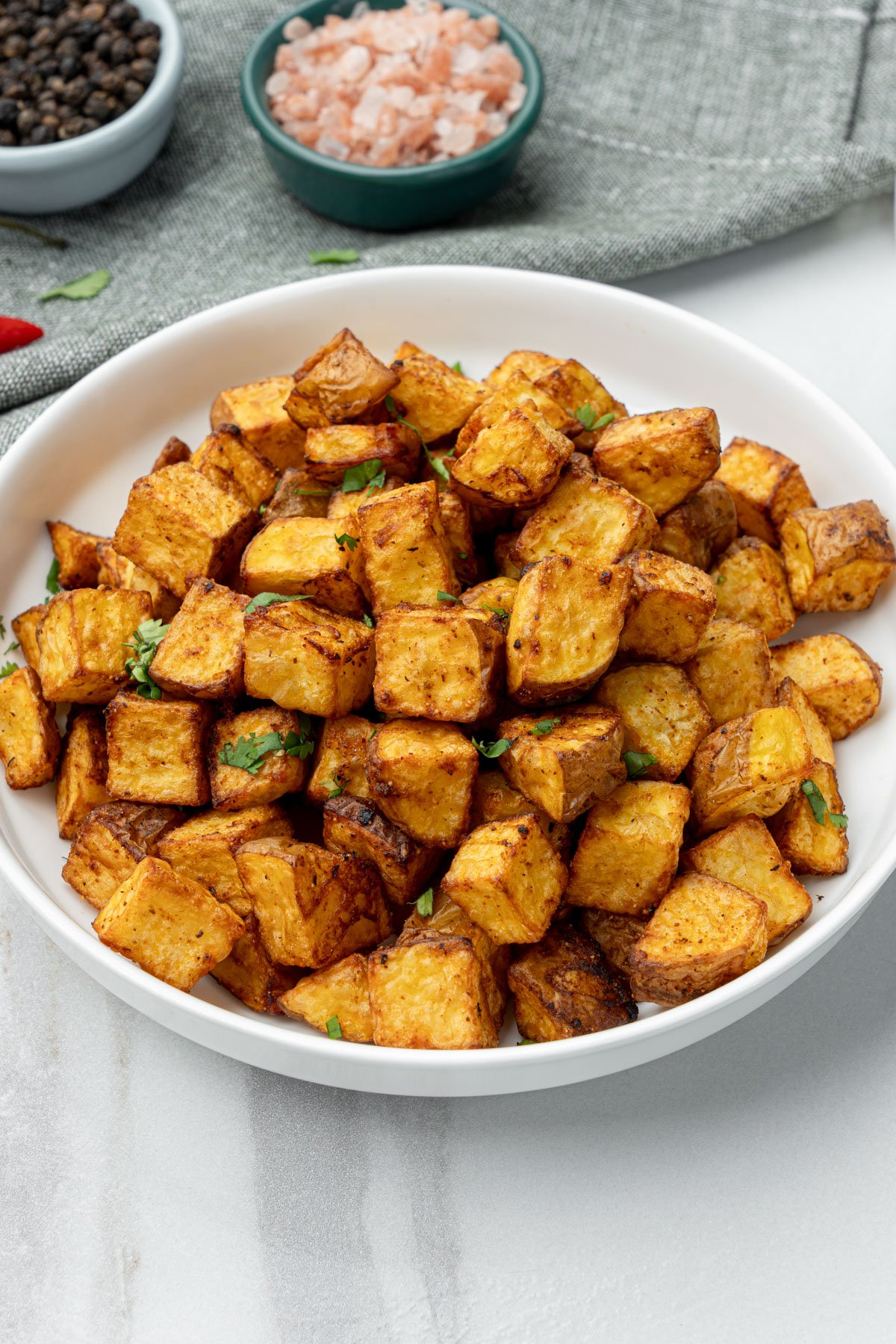 air fryer diced potato in a bowl with salt and pepper at the back