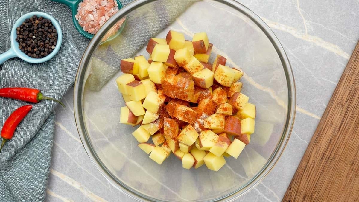 garlic powder and paprika added to diced potato in a bowl to make air fryer diced potato