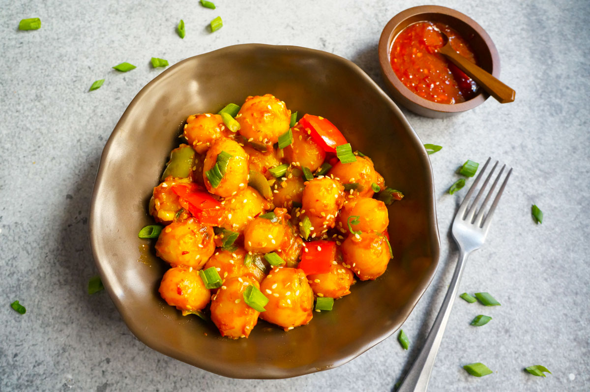 Flavorful and easy Garlic Chili Potatoes, made with steamed potatoes, garlic, chili sauce and honey, sprinkled with green onions and sesame seeds. Enjoy them as an appetizer or side! Garlic chili potatoes in a bowl with chili paste on side