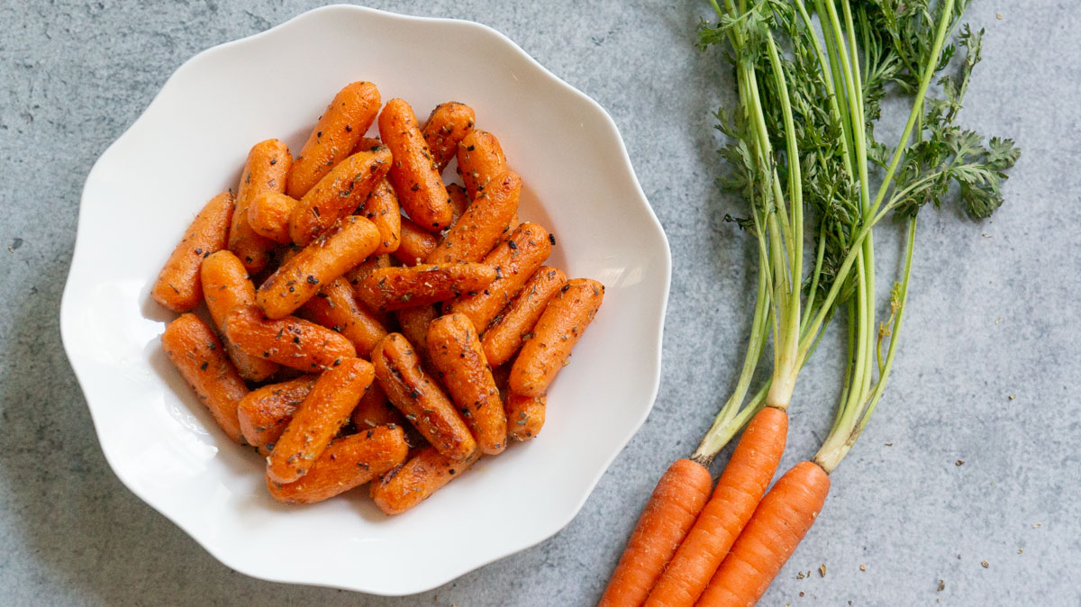 ready to serve Garlic Herb Carrots on a white plate with fresh carrots on side