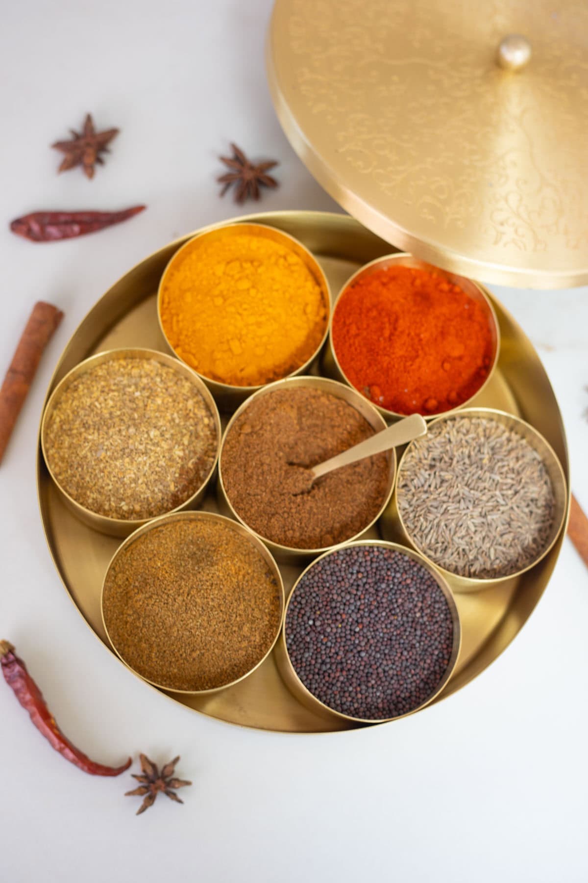 Traditional Indian brass masala dabba with seven compartments filled with spices like turmeric, chili powder, cumin, and mustard seeds.