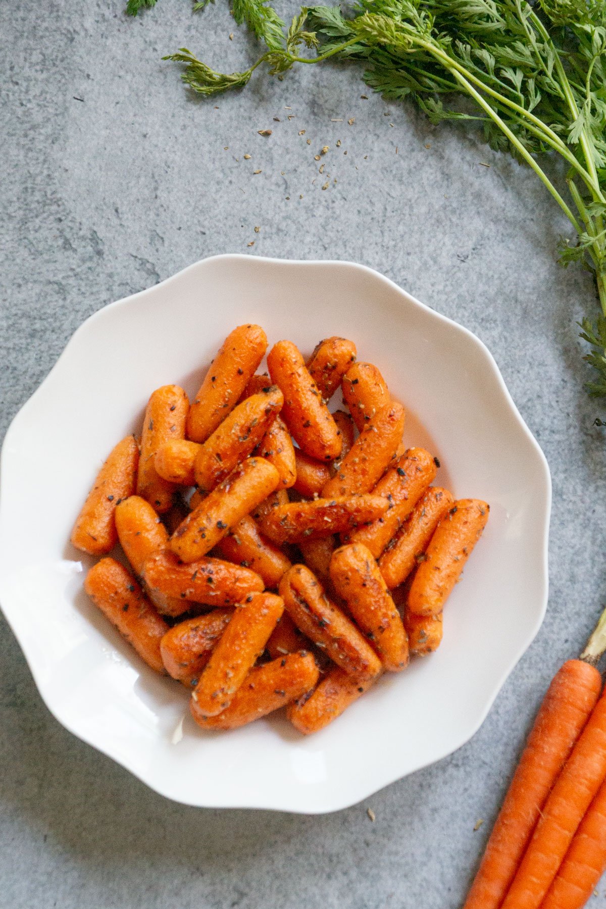 Garlic herb carrots on a plate with fresh carrots on side