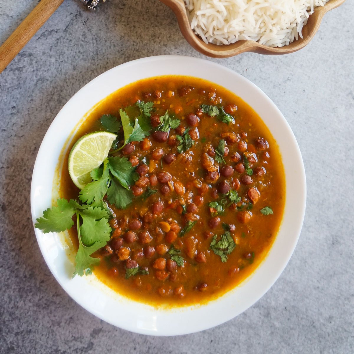 Ready to serve kala chana curry in a white bowl garnished with cilantro and a slice of lime
