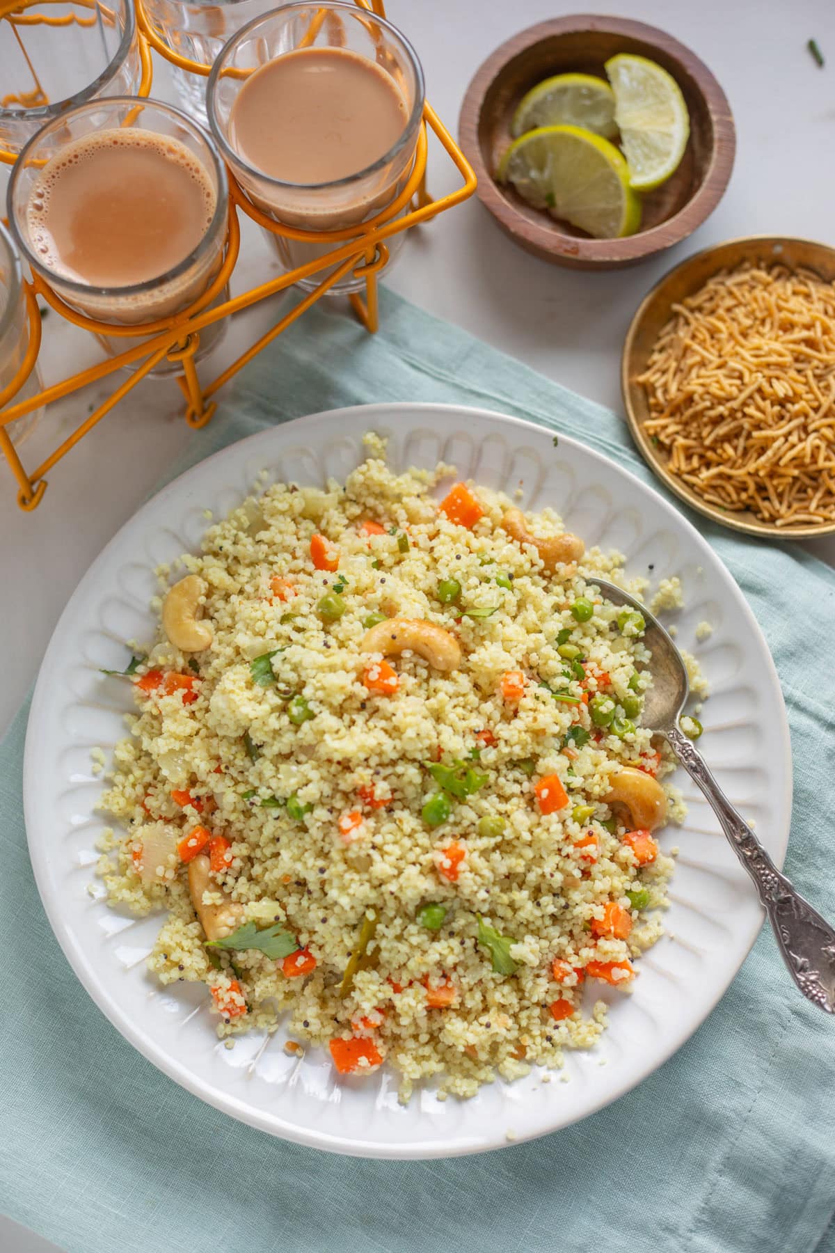 A plate of millet upma with vegetables and cashews, served with chai, lemon slices, and sev