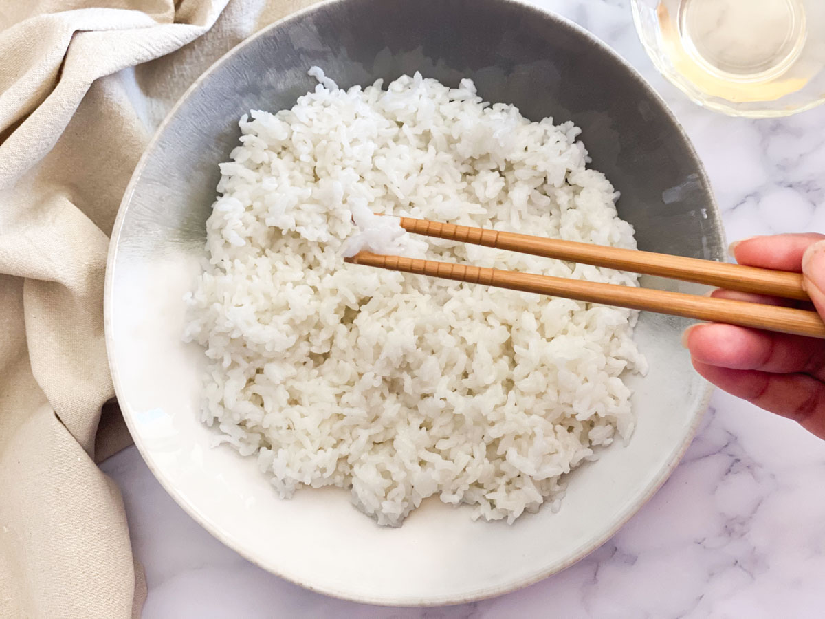 Sushi rice in chopsticks on top of a bowl.