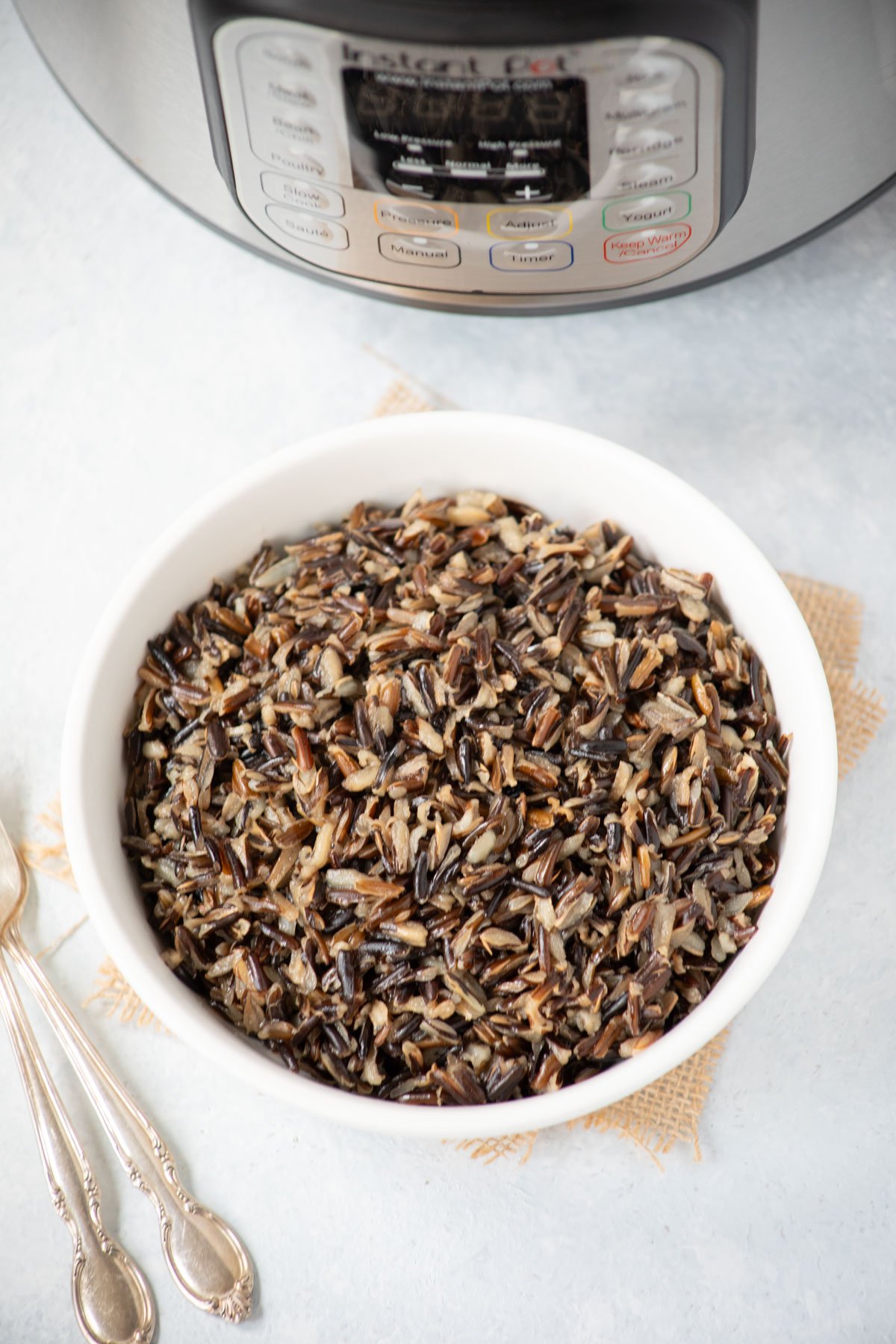 Ready to serve wild rice in a white bowl with instant pot at the back