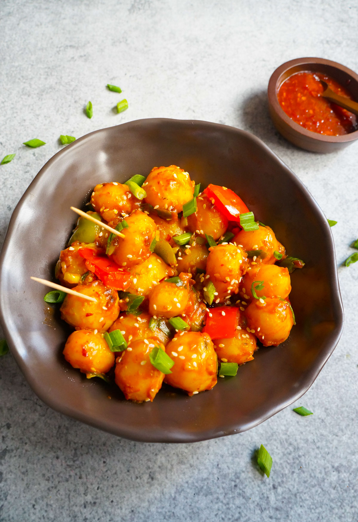 Flavorful and easy Garlic Chili Potatoes, made with steamed potatoes, garlic, chili sauce and honey, sprinkled with green onions and sesame seeds. Enjoy them as an appetizer or side! top view of garlic chili potatoes in a brown bowl