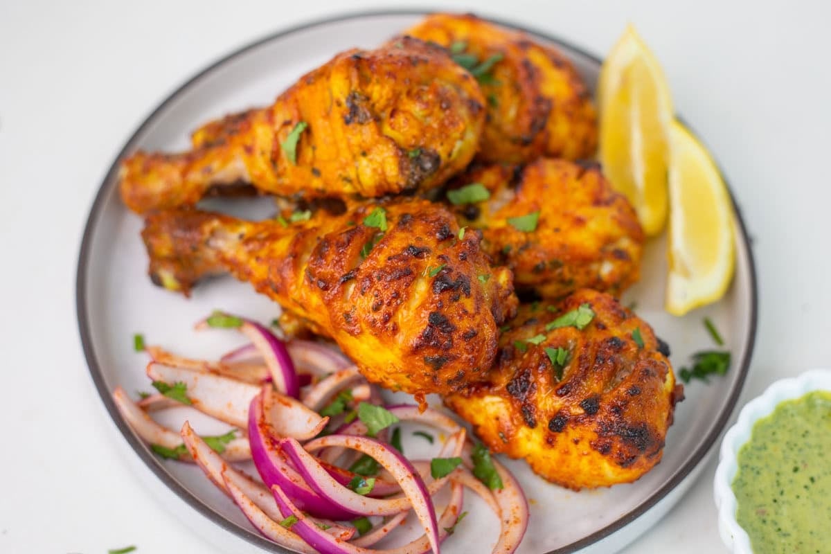 Tandoori chicken legs on a small white plate with onion and lemon slice
