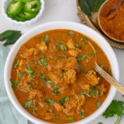 Chicken chettinad in a white bowl with cilantro, pepper and lime slice on side