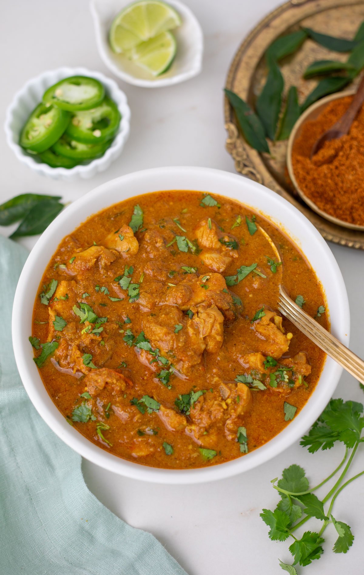 Chicken chettinad in a white bowl with cilantro, pepper and lime slice on side