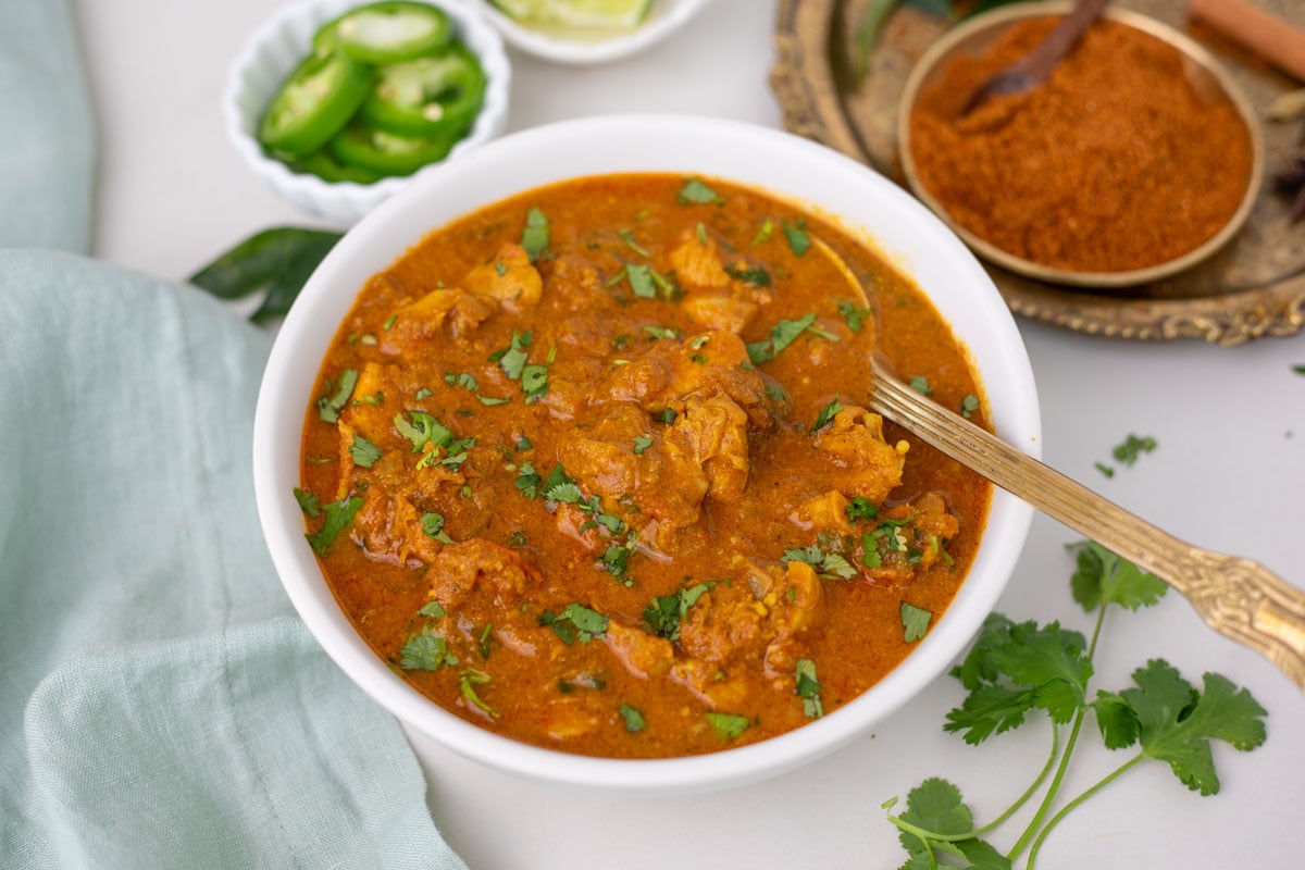 Chicken Chettinad Kulambu in a white bowl with brass spoon