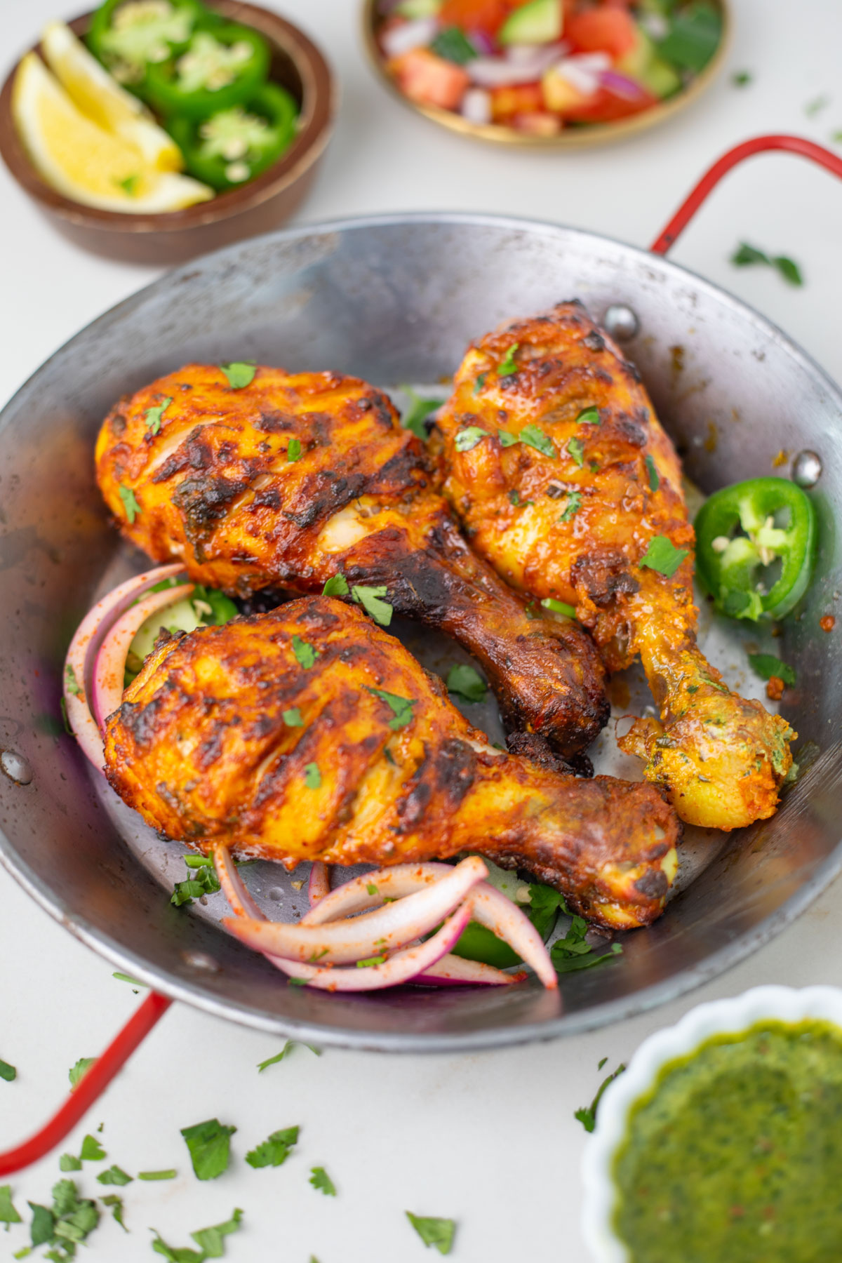 A flavor packed spicy dish from the Indian subcontinent popular all over the world - Tandoori Chicken. Chicken is marinated in yogurt, ginger, garlic, spices and lemon juice, then grilled in the air fryer or oven. Ready to serve air fryer tandoori chicken in a small pot garnished with cilantro, onions and pepper
