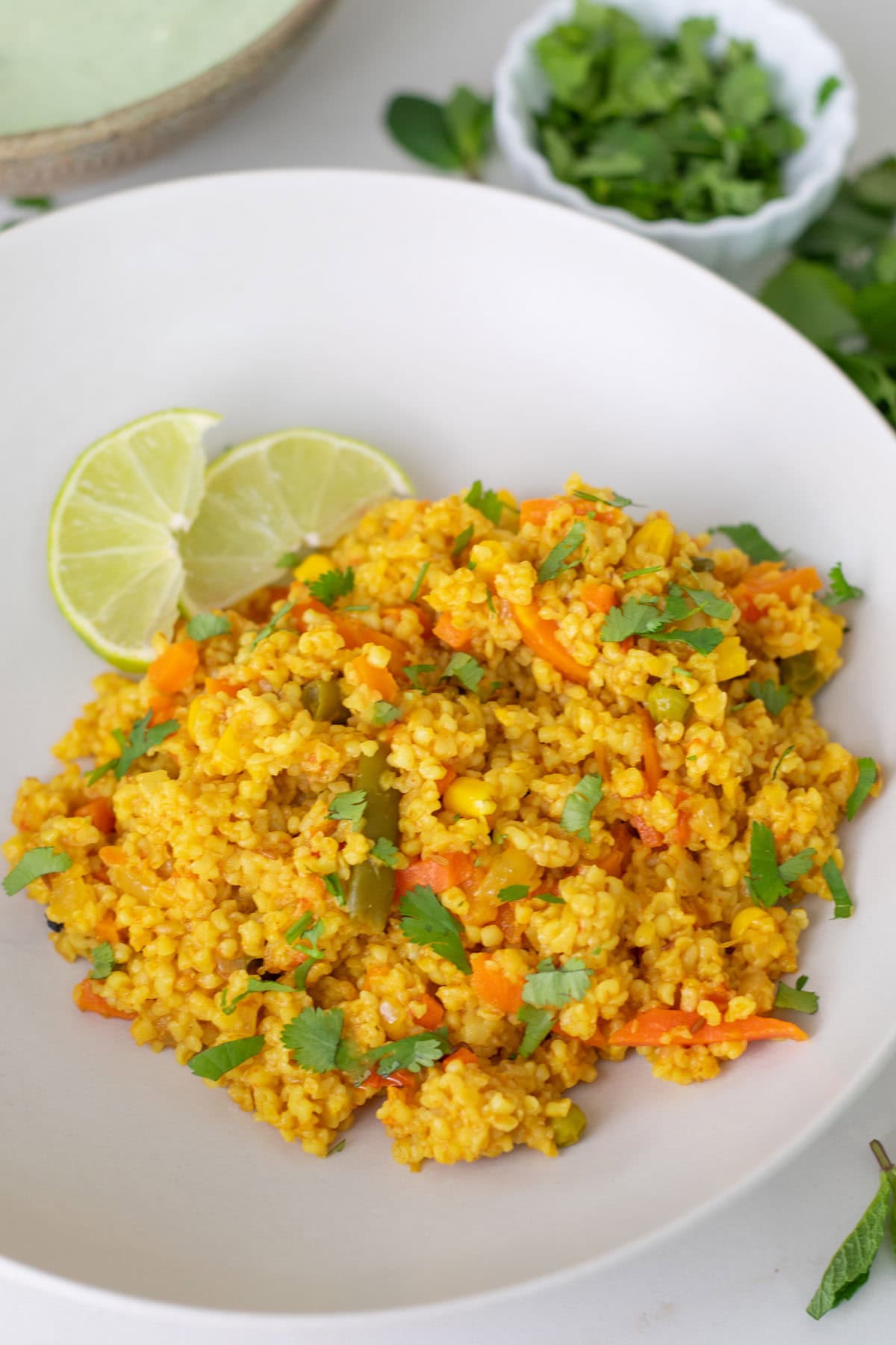 Ready to serve dalia pulao on a white plate garnished with cilantro and lime slice