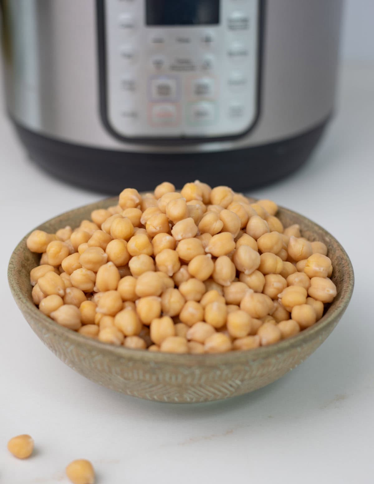 A bowl of tender cooked chickpeas in front of an instant pot.