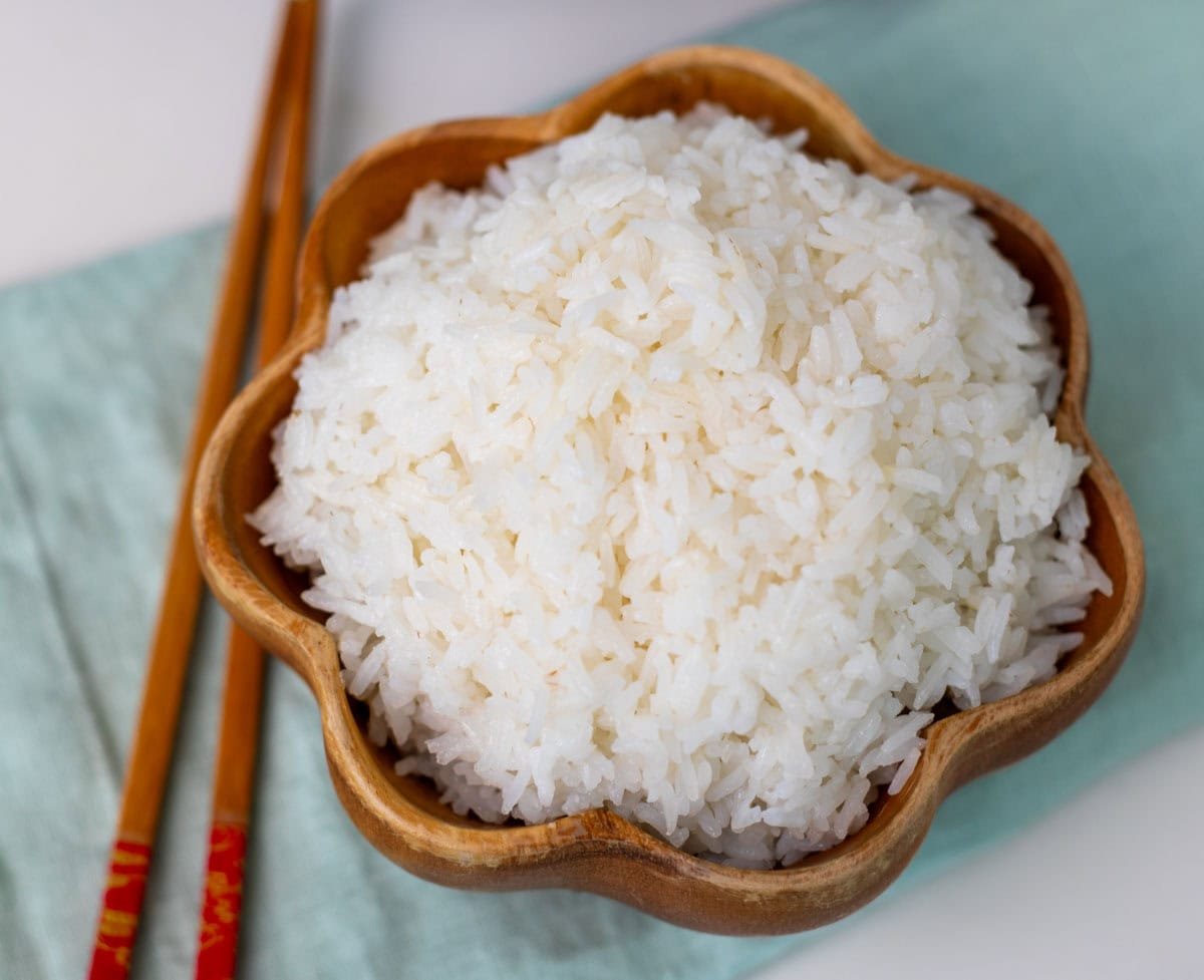 closeup shot of jasmine rice in a wooden bowl with a pair of chopsticks