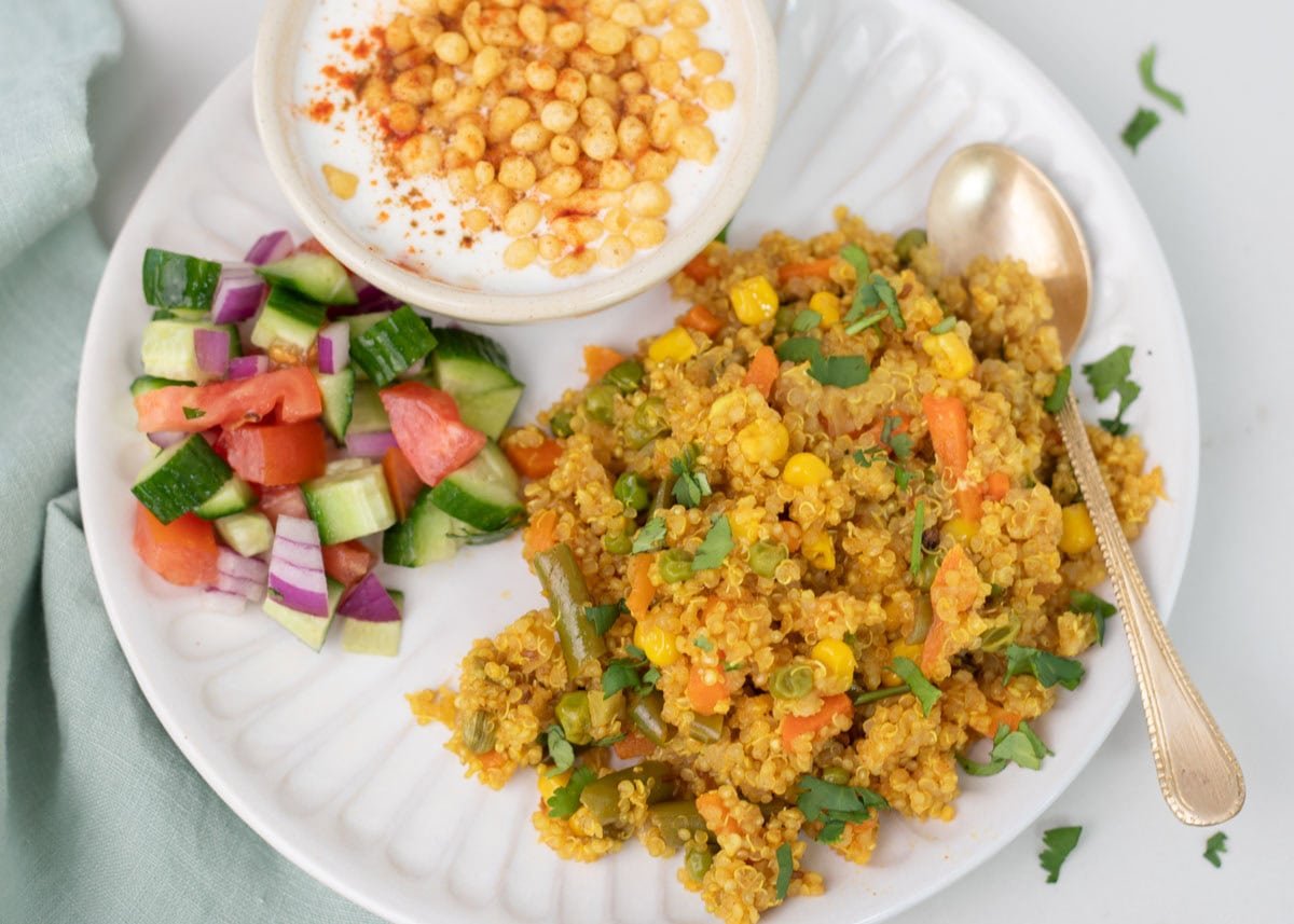 Quinoa pulao with cucumber tomato salad, and raita on a white plate