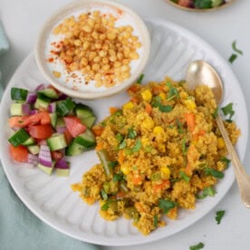 quinoa pilaf with vegetables, cucumber tomato salad, and raita on a white plate