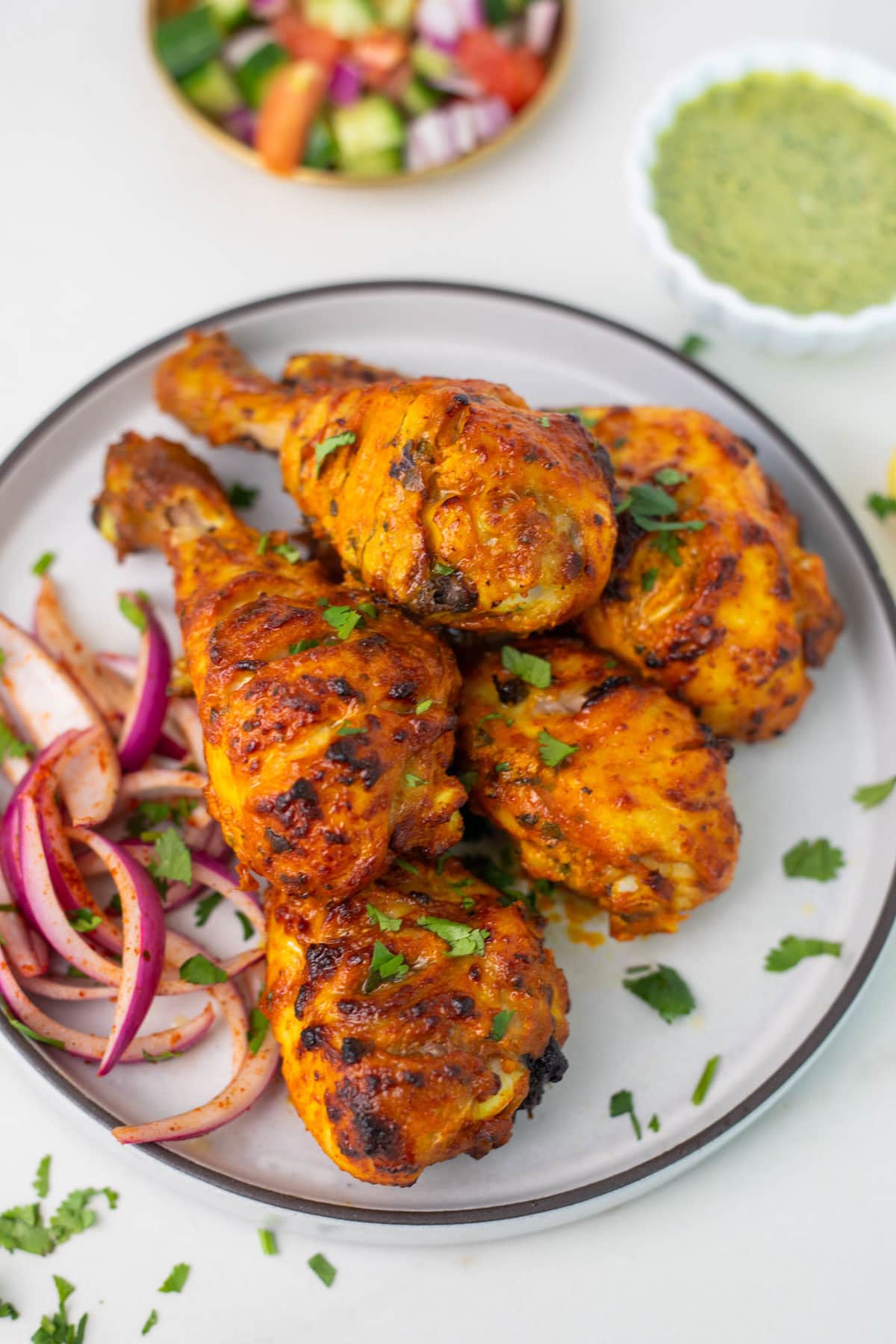 Air fryer tandoori chicken legs on a white plate garnished with cilantro