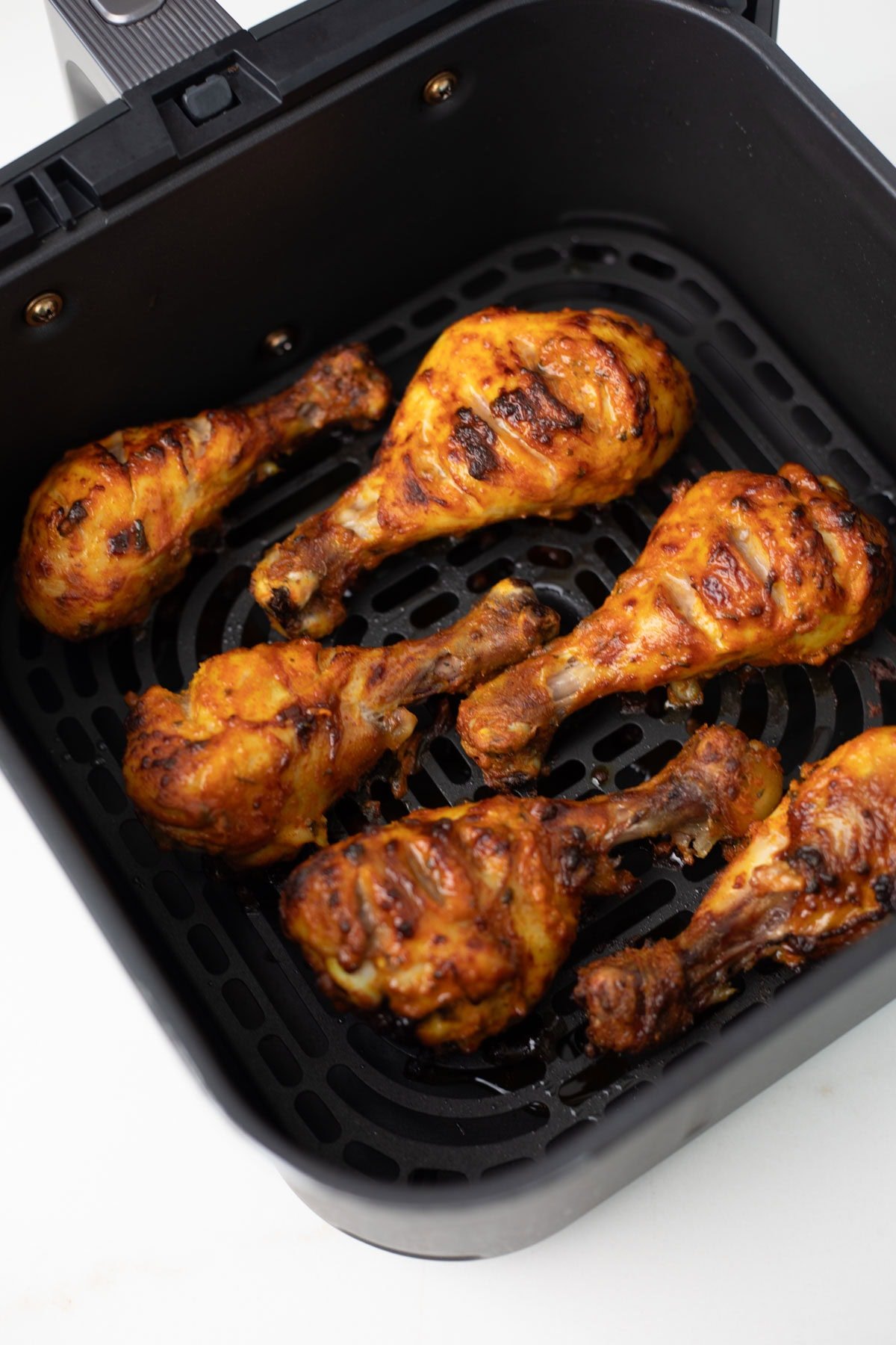A flavor packed spicy dish from the Indian subcontinent popular all over the world - Tandoori Chicken. Chicken is marinated in yogurt, ginger, garlic, spices and lemon juice, then grilled in the air fryer or oven. closeup shot of tandoori chicken in an air fryer basket