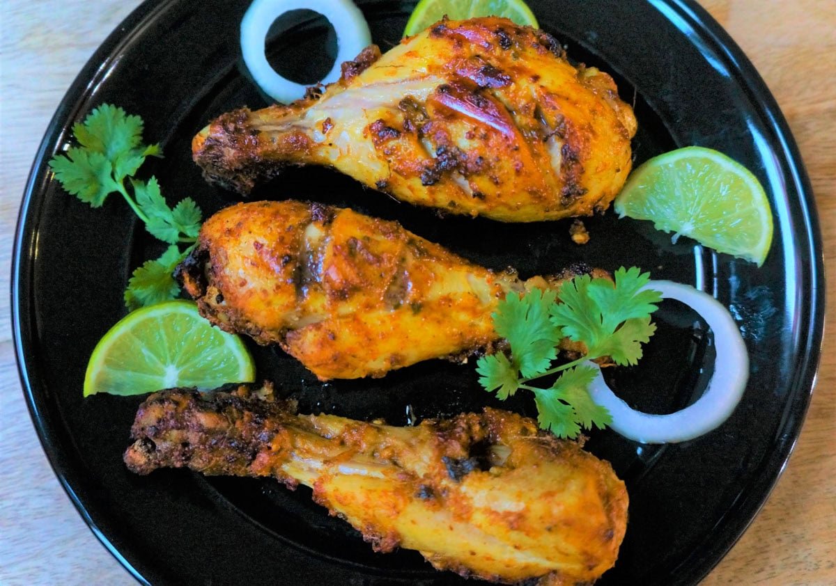 A flavor packed spicy dish from the Indian subcontinent popular all over the world - Tandoori Chicken. Chicken is marinated in yogurt, ginger, garlic, spices and lemon juice, then grilled in the air fryer or oven. top view of air fryer tandoori chicken on a black plate