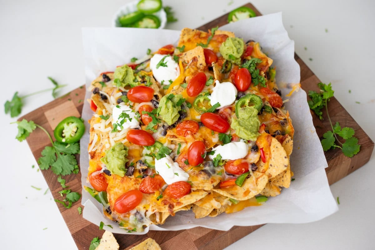 air fried nachos on a wooden chopping board with cilantro and jalapeno on side