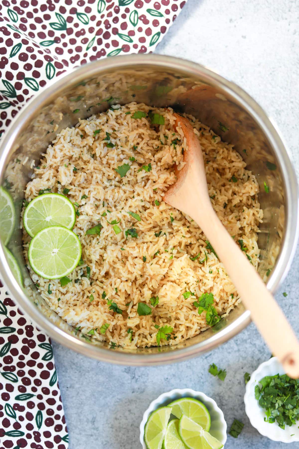 Cilantro Lime Brown Rice cooked in the instant pot, with a ladle and some lime and cilantro in small white bowls