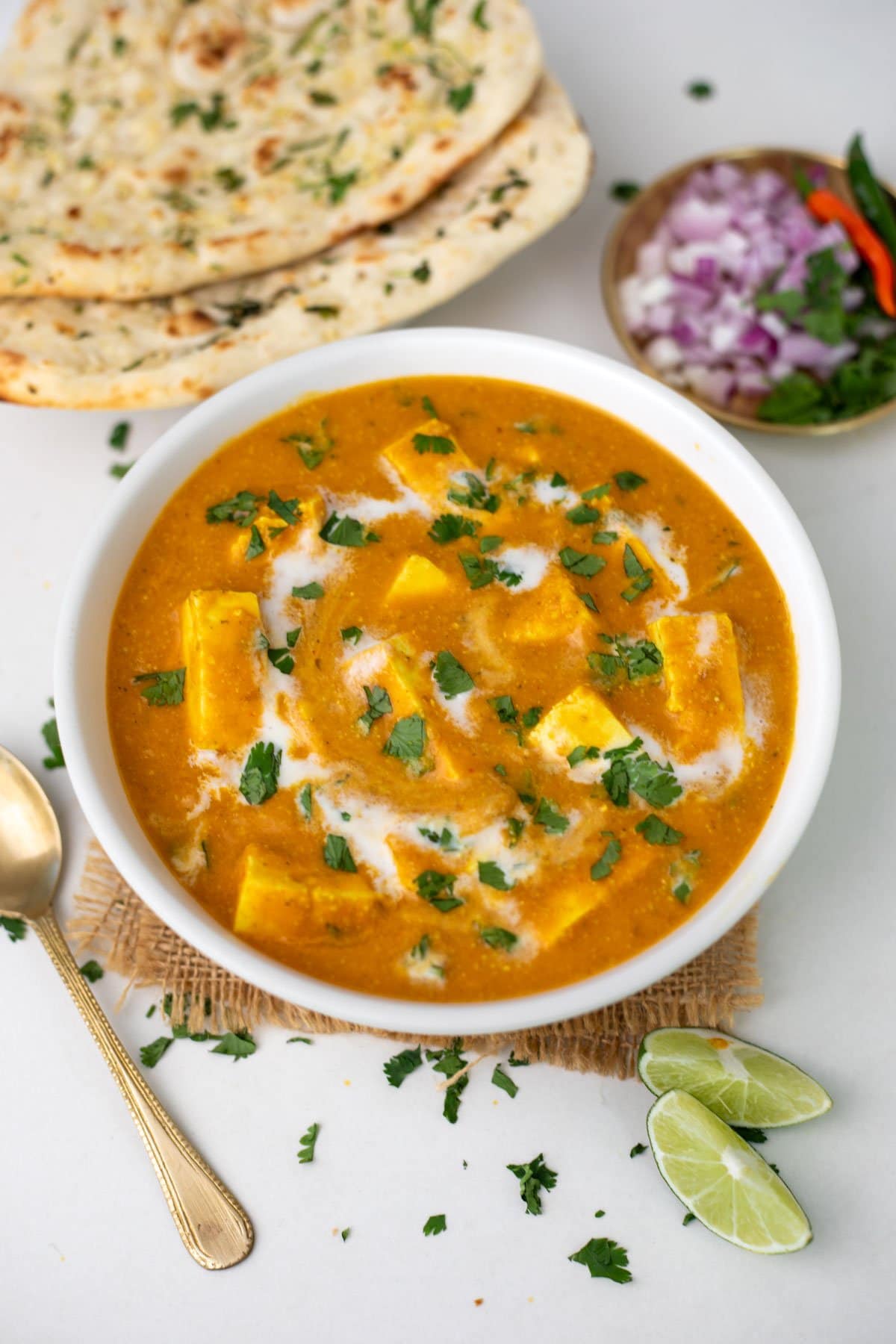 ready to serve paneer butter masala in a white bowl with lime slice and naan bread on side