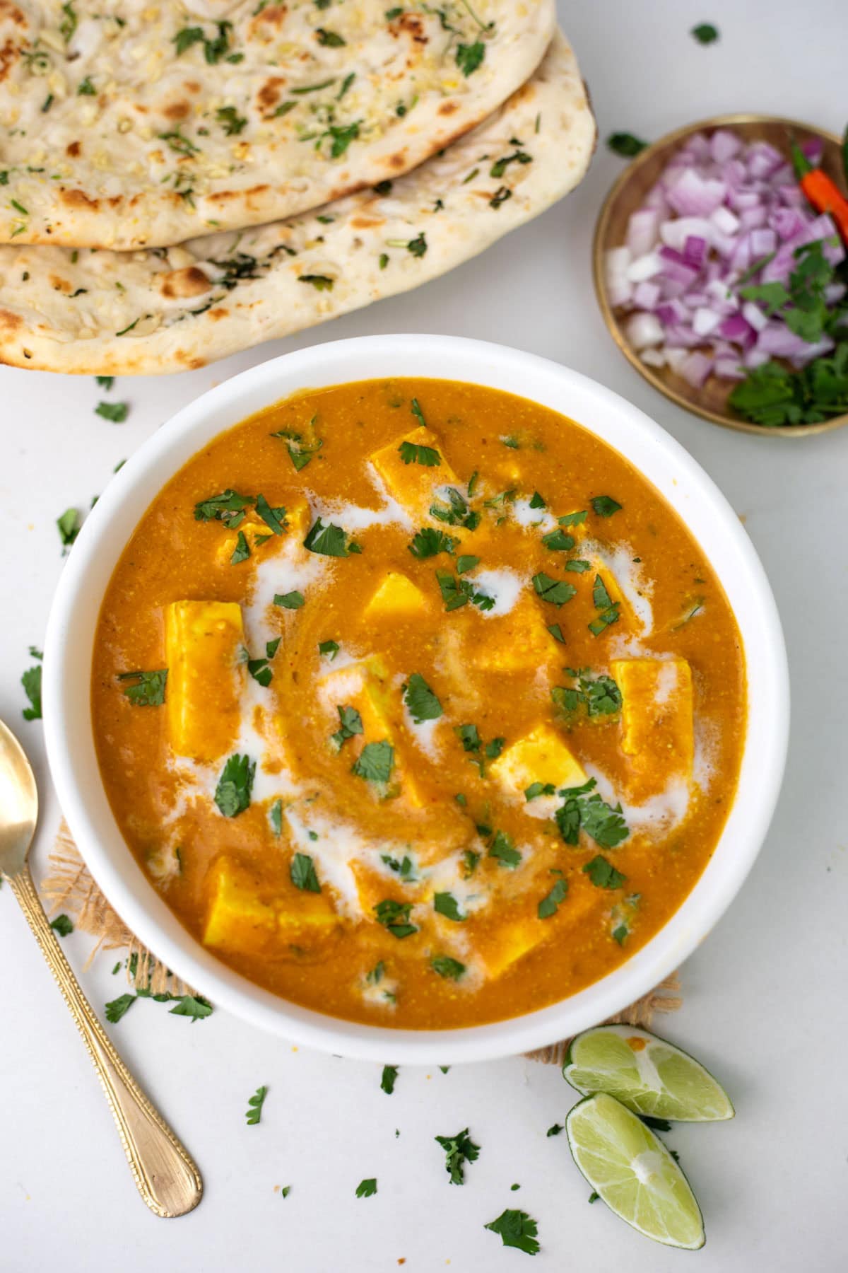 paneer butter masala in a white bowl with naan bread on side