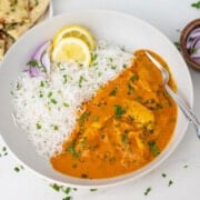 Butter chicken with rice on a plate topped with cilantro