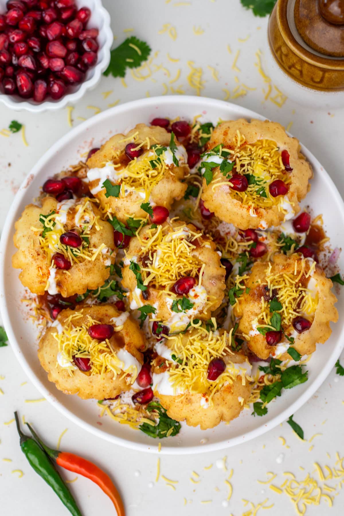 Dahi puri on a white plate topped with pomegranate seeds and cilantro.