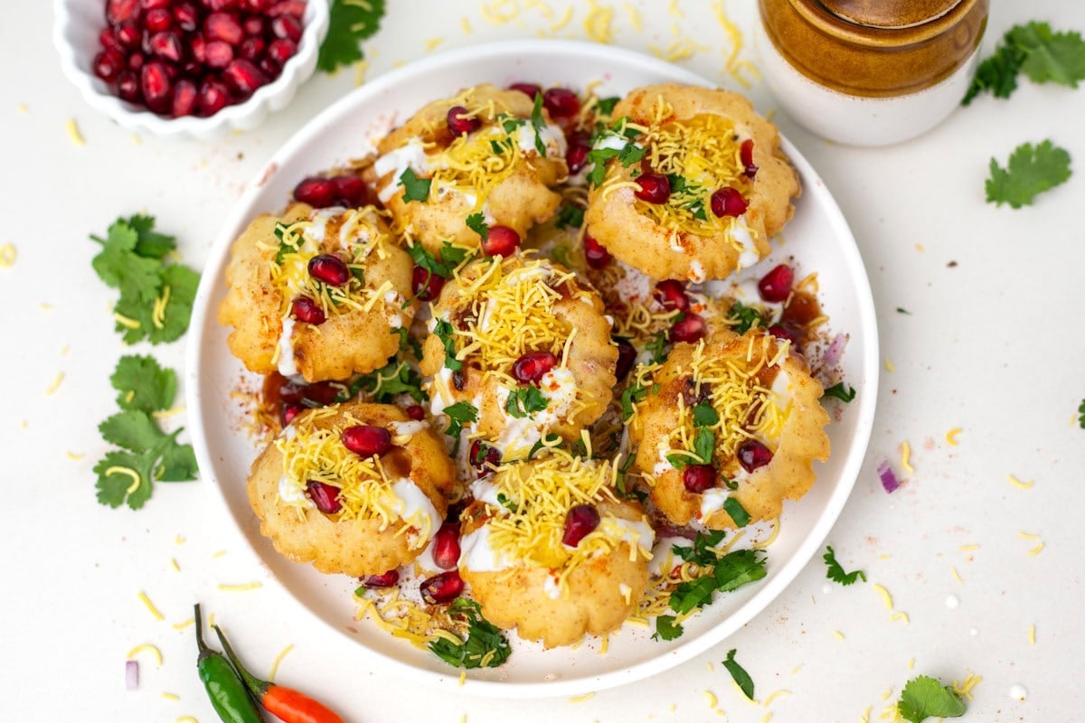 Dahi batata puri on a white plate topped with pomegranate seeds