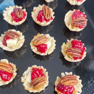 Phyllo Cups topped with brie, cranberry sauce, and pecans on a baking tray.