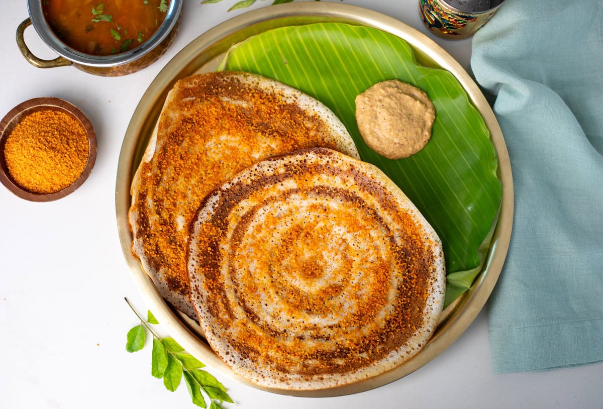Top view of Ghee Podi Dosa on a brass plate with banana leaf and chutney on side