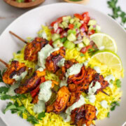 Chicken Tikka Kebab Skewers served over saffron rice with salad and lime on the side.