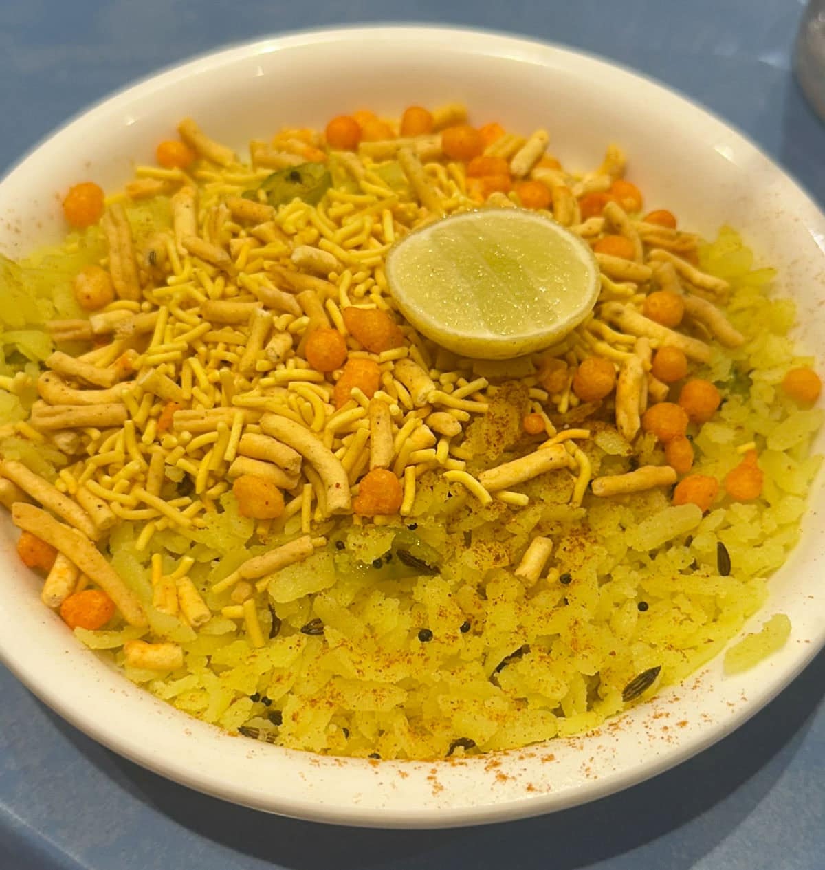 Poha topped with farsan and lime.