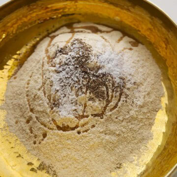 Whole wheat flour with salt, ajwain, and oil in a brass bowl.