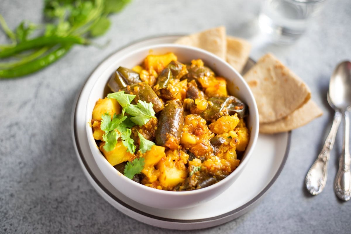 Aloo Baingan made in pressure cooker served in a white bowl with roti on the side.