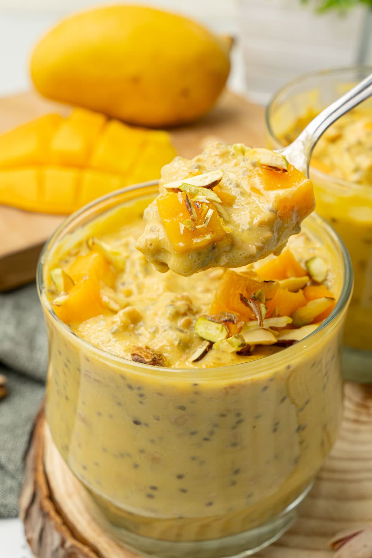 Creamy mango overnight oats with chia seeds in a spoon over a cup.