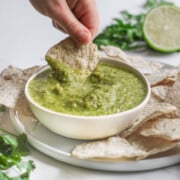 Dipping a tortilla chip into Salsa Verde in a bowl.